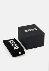 Mustad mustast pappkarbist, millel on suur valge "BOSS" logo, ja sellega kaasas must kangast rahakott sama logo ja väikese kuldse rõngasmärgiga.