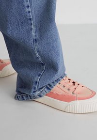 Pink sneaker with textured fabric and white rubber sole, paired with relaxed-fit blue denim jeans featuring a frayed hem.