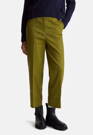 Pantalons ajustés vert olive, à jambe droite et avec des poignets, fabriqués à partir d'un tissu lisse. Portés avec des bottines noires et un pull bleu marine.