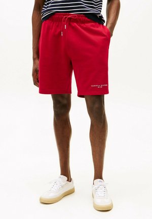 Mand iført røde Tommy Hilfiger-shorts med snøre, kombineret med hvide sneakers og en navy- og hvidstribet skjorte.