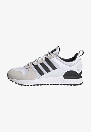 Białe i szare buty sportowe Adidas z czarnymi paskami, wiązane, z teksturowaną podeszwą, widoczne z boku na białym tle.