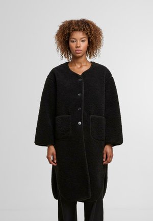 Melnas vilnas mētelis ar apaļu apkakli, lielu pogas aizdari, divām priekšējām kabatām un sānu šķēlumiem vieglākai kustībai. Fakturēts audums.