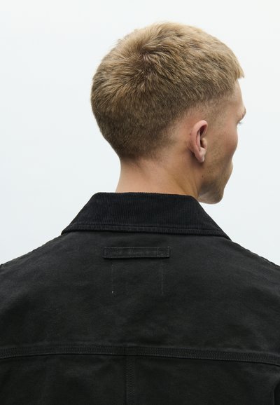 Μαύρο σακάκι από κορδόνι με δομημένο γιακά, ορατή ραφή και οριζόντια υφασμάτινη ετικέτα στο πάνω μέρος της πλάτης.