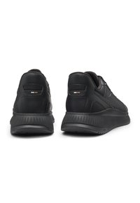 Mustat tennarit, joissa on teksturoitu nahkapäällinen, hienovaraiset pienet reiät, pehmustettu pohja ja minimalistiset yksityiskohdat kantapäässä.