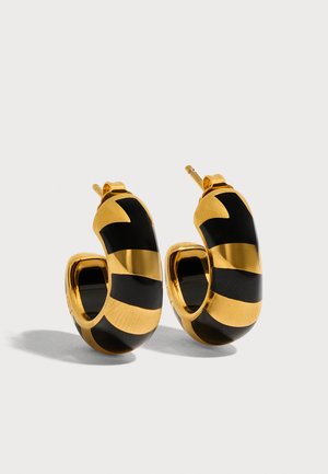 Paire de boucles d’oreilles créoles en or avec motifs de bandes courbes noires et fermoirs à tige sur fond clair.