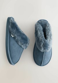 Blauwe suède pantoffels met een zachte, lichtblauwe nepbont voering. Ronde vorm met een platte zool en gestikte details langs de randen.