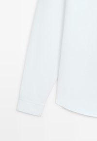 Weißes Langarmhemd teilweise dargestellt, mit glatter Textur, geradem Schnitt und Manschette mit genähter Kante.