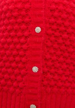Rode gebreide stof met een gestructureerd patroon en een verticale rij van drie ronde strasstenen knopen in een close-up weergave.