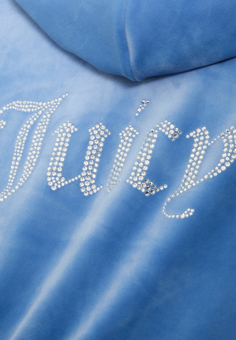 Felpa blu con una texture liscia. Presenta la scritta "Juicy" in strass argentati, con un effetto sfumato nel colore del tessuto.