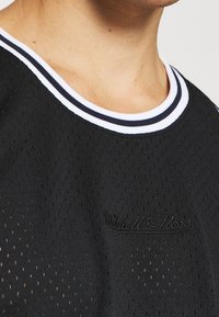 Haut de sport en mesh noir avec un col rond, présentant un bord-côte rayé blanc et marine et un logo embossé sur la poitrine.