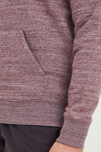 Sudadera color marrón con una tela texturizada, bolsillo tipo canguro, puños y dobladillo acanalados. Presenta un patrón de hilo mezclado.