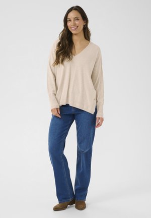 Beige V-hals trøje med lange ærmer, parret med blå lige ben jeans og brune ruskinds ankelstøvler. Glat tekstur, afslappet pasform.
