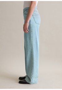 Světlé modré kalhoty s širokými nohavicemi a vysokým pasem, které mají kapsy a mírně vyšisovanou texturu denimu. Látka vypadá měkká a odolná.