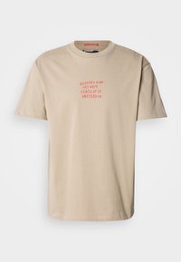 Beige színű pamut póló, kerek nyakkal, rövid ujjal, és vörös színű nyomott felirattal: "SCOTCH & SODA ART DEPT. CLASS OF '85 AMSTERDAM."