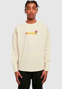 Beige színű pamut sweatshirt hosszú ujjakkal. Az elején sárga és barna színű mese hot dog minta látható. Fekete nadrág.
