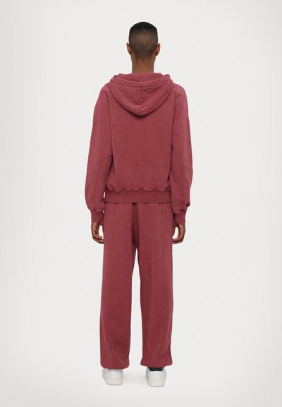 Sweatshirt maroon com capuz ajustável e punhos canelados, emparelhado com calças largas a condizer. Textura de tecido suave, caimento descontraído.