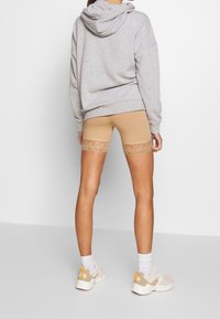 Béžové šortky s ozdobnými krajkovými pásky, šedá mikina s kapucí a světlé tenisky. Je patrná jemná textura a přiléhavý střih.