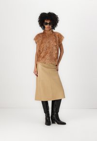 Brun, fuzzy teksturert strikket topp med høy krage og korte ermer, parret med en lys beige, knelengde skinnskjørt og svarte knelange støvler.