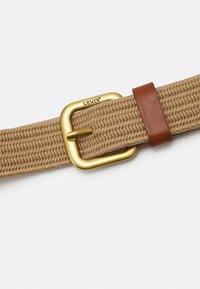 Cinturón de lona en color marrón claro con textura tejida, que cuenta con una hebilla de metal dorado y un acento de cuero marrón. El logo de la marca está impreso en la hebilla.