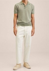 Polo en maille verte à manches courtes et ourlet côtelé, associé à un pantalon ample couleur crème et des baskets beige clair.