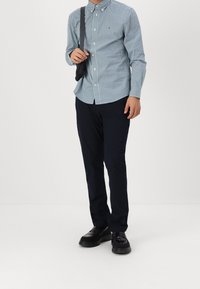 Camicia a quadri blu chiaro e verde, con maniche lunghe, abbinata a pantaloni navy scuri e scarpe nere, che mostrano uno stile casual e aderente.