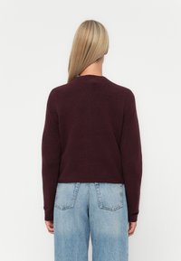 Pull en tricot bordeaux avec un col rond et des manches longues, présentant une coupe décontractée et une texture douce sur un fond uni.