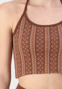 Brun mönstrad kort topp med halterneck, med diamanter och randiga mönster i vitt och ljusbrunt på ett texturerat tyg.
