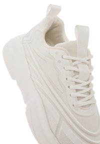 Witte sportieve schoen met een gestructureerde mesh bovenkant en gladde accenten, ronde neus en een dikke zool. Inclusief een trekband aan de hiel.