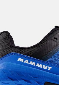 Niebiesko-czarne buty sportowe z siateczkowej cholewki, teksturowanymi akcentami oraz wyraźnym logo "Mammut". Zauważalny detal gumowej podeszwy.