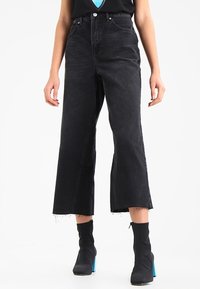 Högmidjade svarta denimjeans med vida ben och fransar i fållen. Har en klassisk femficksdesign och standard dragkedjestängning framtill.