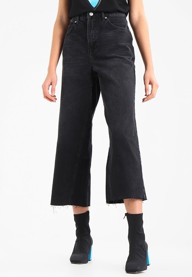 Högmidjade svarta denimjeans med vida ben och fransar i fållen. Har en klassisk femficksdesign och standard dragkedjestängning framtill.