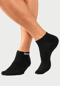 Calcetines negros hasta el tobillo, hechos de un material suave y elástico. Presentan un puño acanalado y un pequeño logotipo de la marca en blanco en el costado.