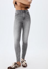 Vaqueros ajustados de cintura alta en gris, con textura suave y diseño de cinco bolsillos, que presentan un sutil desgaste y cierre frontal con botones.