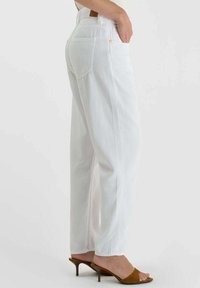 Witte spijkerbroeken met een losse pasvorm, met een hoge taille, achterzakken en subtiele stiksel details, gecombineerd met bruine sandalen met hak.