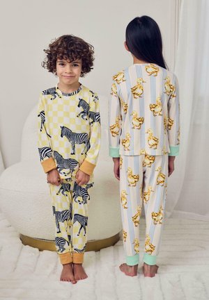 Niño de frente con pijama amarilla con estampados de cebra, niña de espaldas con pijama blanca con estampados de patos y rayas verticales azules.