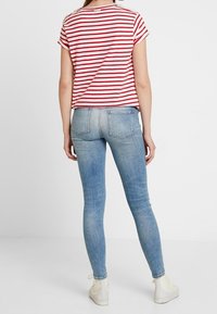 Top de rayas rojas y blancas de manga corta combinado con jeans ajustados de color azul claro, con un corte estándar y mínimo desgaste.