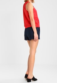 Röd ärmlös topp med spetstillbehör i nederkant, kombinerad med marinblå shorts med scallopkant och svarta öppna hälskor.