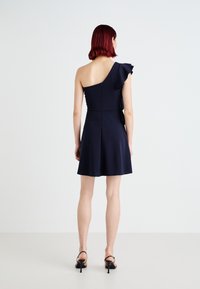 Vestido azul-marinho de um ombro com detalhe em babado. Corpinho justo, saia rodada e um zíper discreto nas costas. Textura de tecido suave.