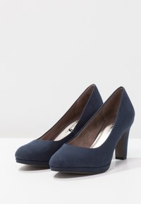 Escarpins en daim bleu marine, à bout arrondi, texture lisse et talon épais. Intérieur doublé de tissu argenté, design minimaliste.