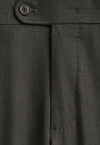 Primo piano di pantaloni grigio scuro su misura con bottone frontale e pieghe, che mette in risalto la trama del tessuto e i dettagli delle cuciture.