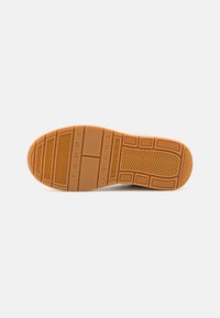 Semelle en caoutchouc de sneakers de couleur tan avec des motifs de semelle prononcés, marque "TOMMY JEANS" en relief, et sections texturées pour une meilleure adhérence.
