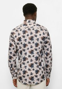 Long-sleeve shirt in light beige with blue and brown floral pattern. Features a classic collar and buttoned cuffs. Smooth fabric texture.