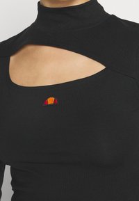 Svart lång ärmad topp med hög krage och ett öppet utskärning vid bröstet. Har en liten, färgglad broderad logotyp på vänster sida.