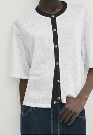 Weißes kurzärmliges Oberteil mit einer schwarzen Knopfleiste und Ausschnitt, ausgestattet mit metallischen Knöpfen und einem lässigen Schnitt. Der Stoff wirkt leicht und strukturiert.