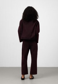 Burgundyröd denimjacka och matchande vida byxor, med en kortad skärning, minimal metalldetaljer och en slät yta med bakfickor.