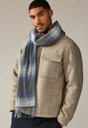 Gray woolen scarf with blue and gray plaid pattern, draped loosely around the neck, paired with a gray jacket featuring a chest pocket.
