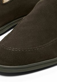 Dark brown suede slipper with a smooth texture, low-profile design, and contrasting stitching along the edges. Soft interior lining.