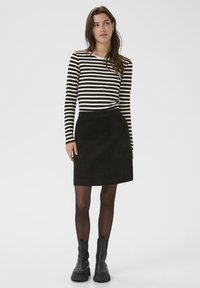 Čierna kordová sukňa s priliehavým pásom a rovnou siluetou, v kombinácii s čierno-bielym pruhovaným topom s dlhým rukávom. Čierne členkové čižmy.