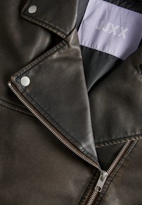 Black leather biker jacket with silver zipper and snap buttons, showing the inside collar label with "JJXX" branding on a gray patch.