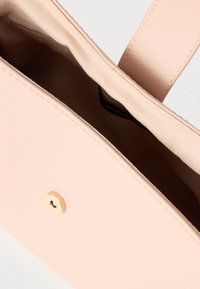 Svetloružová taška cez rameno s textúrovaným povrchom, s horným otvorom a zlatými kovovými detailmi na zapínaní, vystlaná jemným béžovým vnútrom.